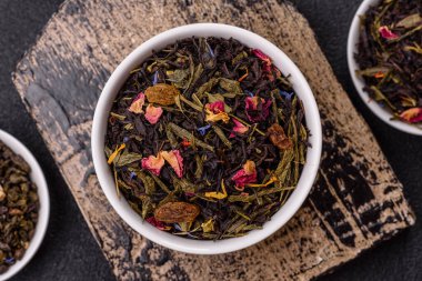 Kuru çay karışımı, koyu beton arka planda siyah, yeşil ve çiçek yaprakları.