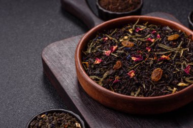 Kuru çay karışımı, koyu beton arka planda siyah, yeşil ve çiçek yaprakları.