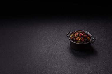 Kuru çay karışımı, koyu beton arka planda siyah, yeşil ve çiçek yaprakları.