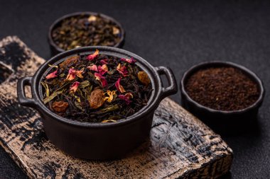 Kuru çay karışımı, koyu beton arka planda siyah, yeşil ve çiçek yaprakları.