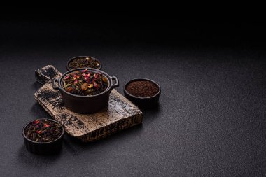 Kuru çay karışımı, koyu beton arka planda siyah, yeşil ve çiçek yaprakları.