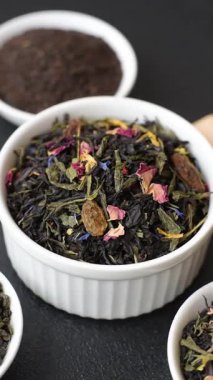 Kuru çay karışımı, koyu beton arka planda siyah, yeşil ve çiçek yaprakları.