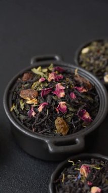 Kuru çay karışımı, koyu beton arka planda siyah, yeşil ve çiçek yaprakları.