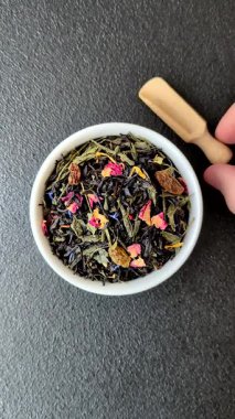 Kuru çay karışımı, koyu beton arka planda siyah, yeşil ve çiçek yaprakları.