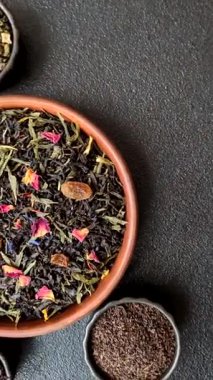 Kuru çay karışımı, koyu beton arka planda siyah, yeşil ve çiçek yaprakları.