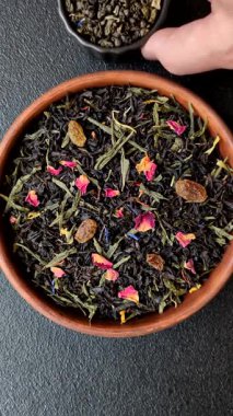 Kuru çay karışımı, koyu beton arka planda siyah, yeşil ve çiçek yaprakları.