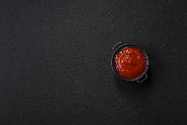 Koyu beton zemin üzerinde seramik sos teknesinde tuz ve baharatlı kırmızı sos ya da ketçap.