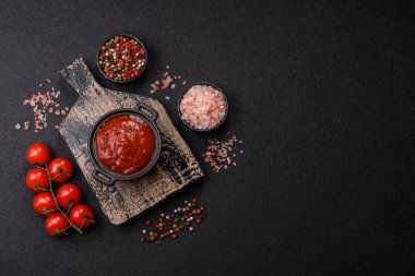 Koyu beton zemin üzerinde seramik sos teknesinde tuz ve baharatlı kırmızı sos ya da ketçap.