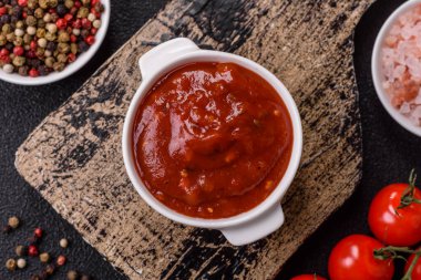 Koyu beton zemin üzerinde seramik sos teknesinde tuz ve baharatlı kırmızı sos ya da ketçap.