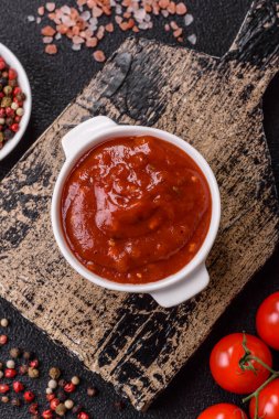 Koyu beton zemin üzerinde seramik sos teknesinde tuz ve baharatlı kırmızı sos ya da ketçap.