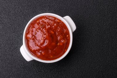 Koyu beton zemin üzerinde seramik sos teknesinde tuz ve baharatlı kırmızı sos ya da ketçap.