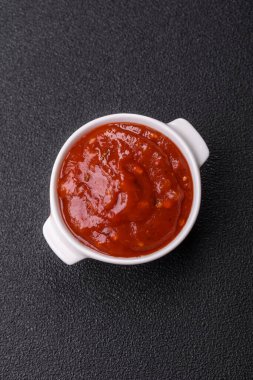 Koyu beton zemin üzerinde seramik sos teknesinde tuz ve baharatlı kırmızı sos ya da ketçap.