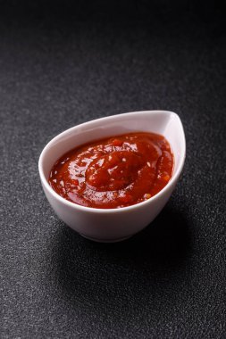 Koyu beton zemin üzerinde seramik sos teknesinde tuz ve baharatlı kırmızı sos ya da ketçap.