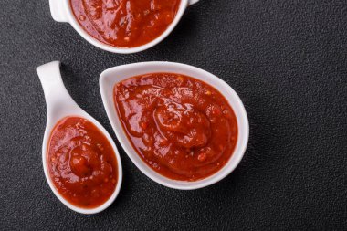 Koyu beton zemin üzerinde seramik sos teknesinde tuz ve baharatlı kırmızı sos ya da ketçap.