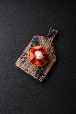 Çilek parçalı yuvarlak tatlı tart ve koyu beton arka planda krema