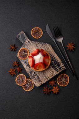 Çilek parçalı yuvarlak tatlı tart ve koyu beton arka planda krema