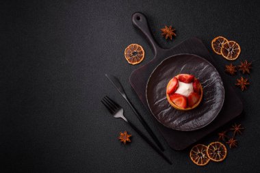 Çilek parçalı yuvarlak tatlı tart ve koyu beton arka planda krema