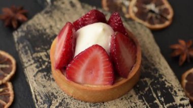 Çilek parçalı yuvarlak tatlı tart ve koyu beton arka planda krema