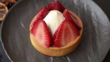 Çilek parçalı yuvarlak tatlı tart ve koyu beton arka planda krema