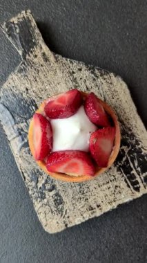 Çilek parçalı yuvarlak tatlı tart ve koyu beton arka planda krema