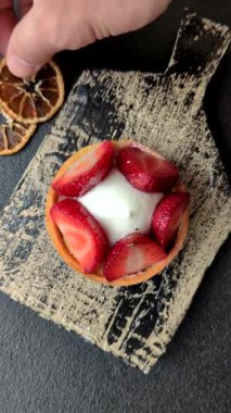Çilek parçalı yuvarlak tatlı tart ve koyu beton arka planda krema