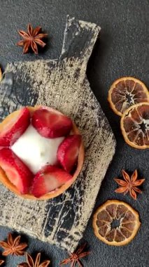 Çilek parçalı yuvarlak tatlı tart ve koyu beton arka planda krema