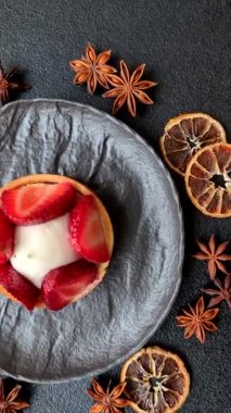 Çilek parçalı yuvarlak tatlı tart ve koyu beton arka planda krema