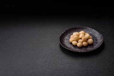 Koyu beton arka planda seramik kasede soyulmuş macadamia cevizi. Besin kaynağı olarak fındık
