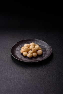 Koyu beton arka planda seramik kasede soyulmuş macadamia cevizi. Besin kaynağı olarak fındık