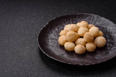 Koyu beton arka planda seramik kasede soyulmuş macadamia cevizi. Besin kaynağı olarak fındık