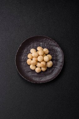 Koyu beton arka planda seramik kasede soyulmuş macadamia cevizi. Besin kaynağı olarak fındık