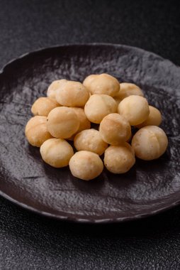 Koyu beton arka planda seramik kasede soyulmuş macadamia cevizi. Besin kaynağı olarak fındık