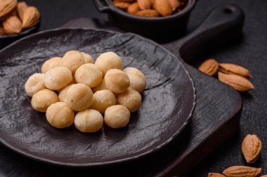 Koyu beton arka planda seramik kasede soyulmuş macadamia cevizi. Besin kaynağı olarak fındık