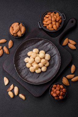 Koyu beton arka planda seramik kasede soyulmuş macadamia cevizi. Besin kaynağı olarak fındık