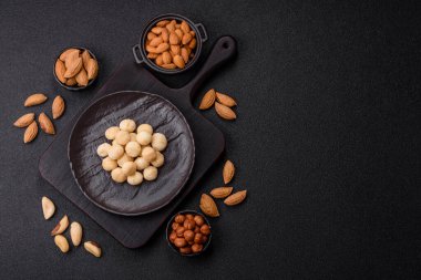 Koyu beton arka planda seramik kasede soyulmuş macadamia cevizi. Besin kaynağı olarak fındık