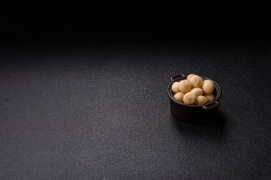 Koyu beton arka planda seramik kasede soyulmuş macadamia cevizi. Besin kaynağı olarak fındık