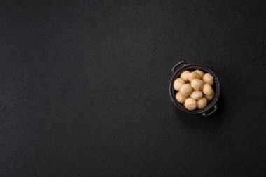 Koyu beton arka planda seramik kasede soyulmuş macadamia cevizi. Besin kaynağı olarak fındık