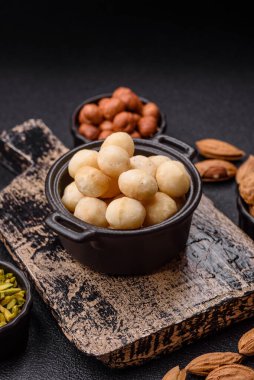 Koyu beton arka planda seramik kasede soyulmuş macadamia cevizi. Besin kaynağı olarak fındık