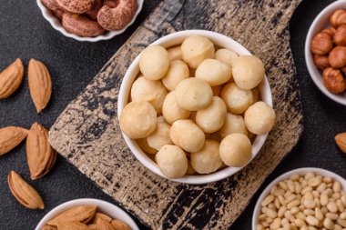 Koyu beton arka planda seramik kasede soyulmuş macadamia cevizi. Besin kaynağı olarak fındık