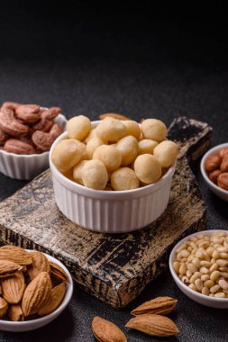 Koyu beton arka planda seramik kasede soyulmuş macadamia cevizi. Besin kaynağı olarak fındık