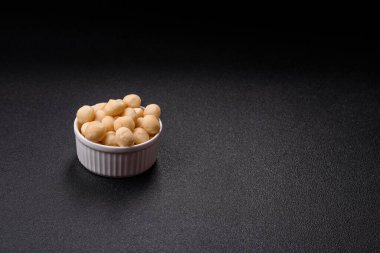 Koyu beton arka planda seramik kasede soyulmuş macadamia cevizi. Besin kaynağı olarak fındık