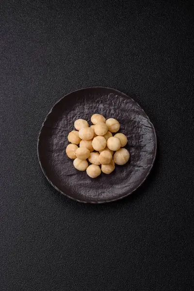 Koyu beton arka planda seramik kasede soyulmuş macadamia cevizi. Besin kaynağı olarak fındık