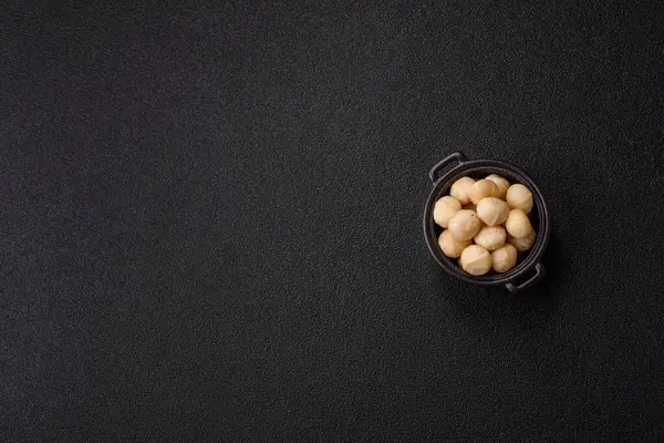 Koyu beton arka planda seramik kasede soyulmuş macadamia cevizi. Besin kaynağı olarak fındık