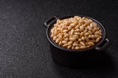 Koyu beton arka planda bir kasede soyulmuş çam fıstığı. Protein kaynağı olarak fındık.