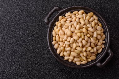 Koyu beton arka planda bir kasede soyulmuş çam fıstığı. Protein kaynağı olarak fındık.