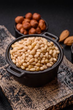 Koyu beton arka planda bir kasede soyulmuş çam fıstığı. Protein kaynağı olarak fındık.