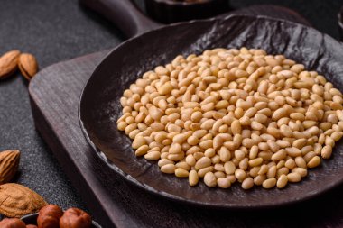 Koyu beton arka planda bir kasede soyulmuş çam fıstığı. Protein kaynağı olarak fındık.