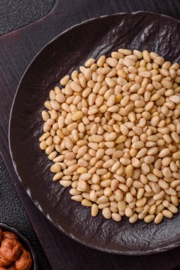 Koyu beton arka planda bir kasede soyulmuş çam fıstığı. Protein kaynağı olarak fındık.