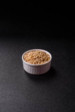 Koyu beton arka planda bir kasede soyulmuş çam fıstığı. Protein kaynağı olarak fındık.