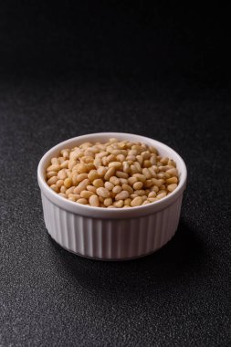 Koyu beton arka planda bir kasede soyulmuş çam fıstığı. Protein kaynağı olarak fındık.